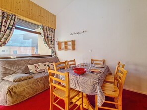 A dining area with a wooden table set for four, surrounded by wooden chairs. - Two-room apartment, mountain view - 4 guests (Les Menuires)