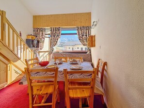 Uma sala de jantar com mesa posta para quatro pessoas, cadeiras de madeira e vista para edifícios através de uma janela com cortinas.
