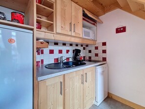 A compact kitchen with wooden cabinets, a white refrigerator, a microwave, and a coffee maker. - Two-room apartment, mountain view - 4 guests (Les Menuires)