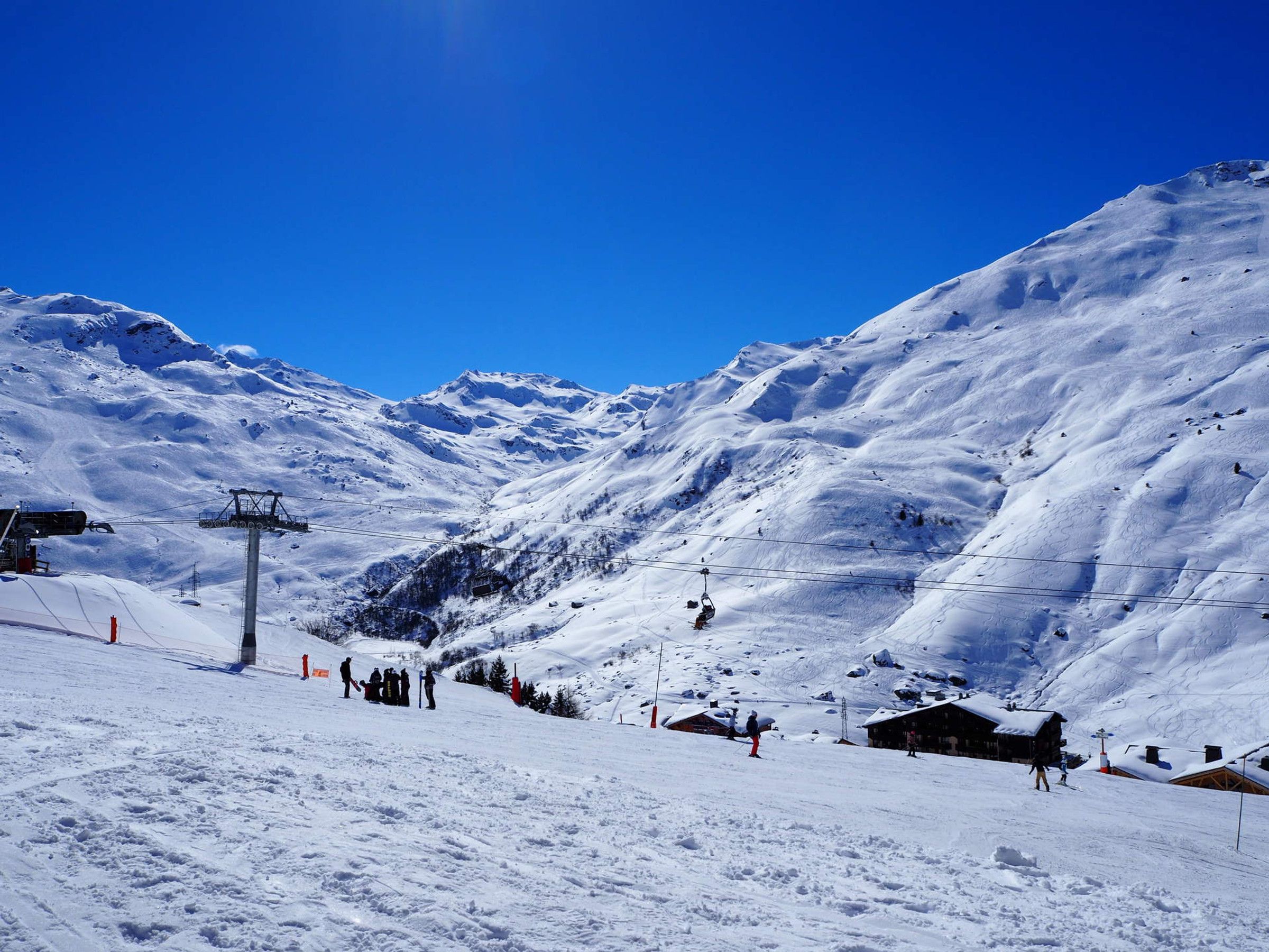 Ein mit Schnee bedeckter Berg mit einer Seilbahn, einer Holzhütte und blauem Himmel.