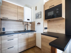 A modern kitchen with wooden cabinets, a black countertop, a built-in microwave, and a water heater. - Mountain studio - 4 guests (Saint-Lary-Soulan)