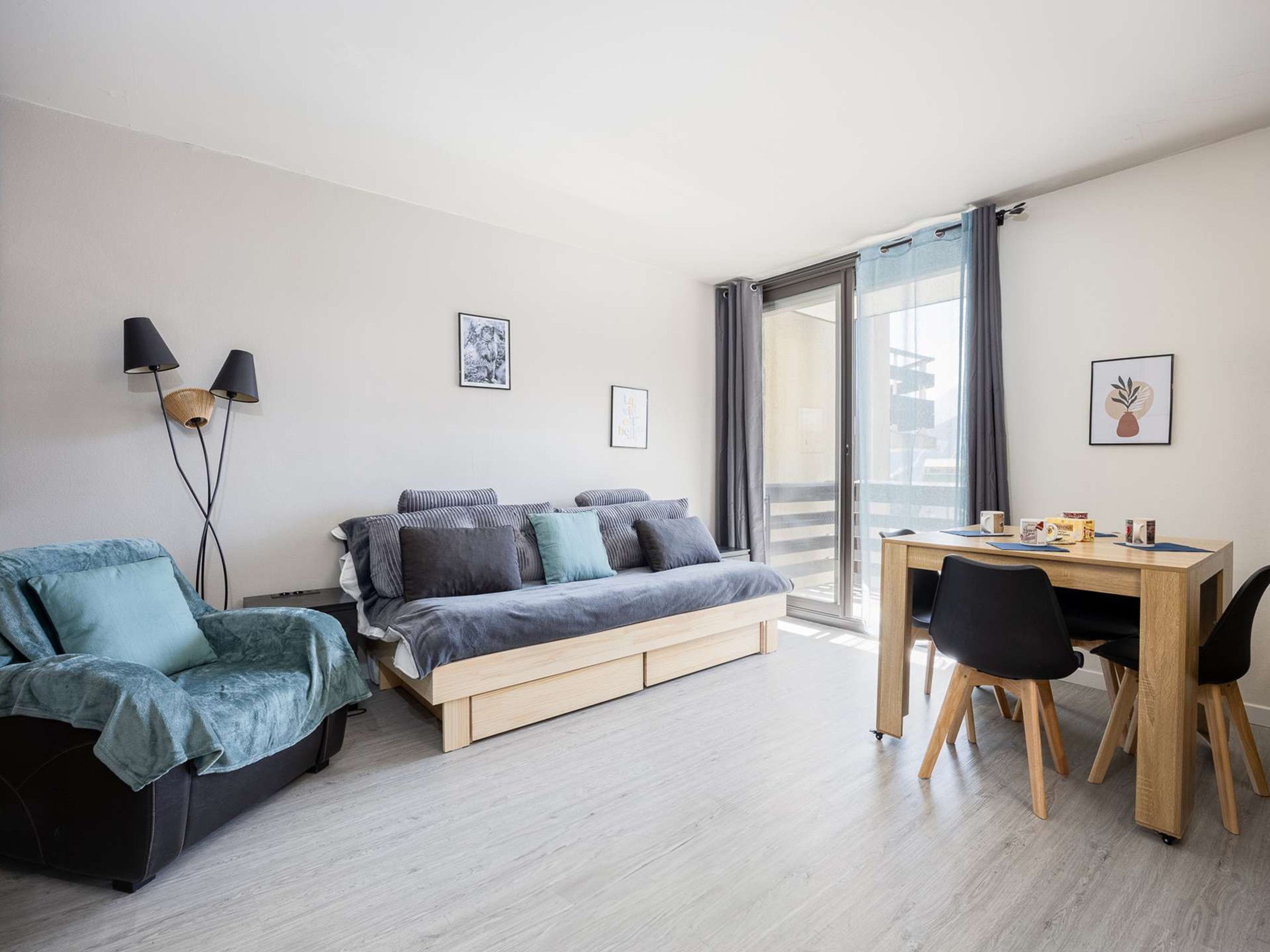 Une chambre moderne avec un lit, un canapé, un bureau et une chaise. Deux lampes sont fixées au mur, et des tableaux encadrés ornent également le mur.