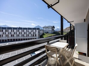 A balcony with a table and chairs, overlooking a road and buildings with a mountain in the background. - Mountain studio - 4 guests (Saint-Lary-Soulan)