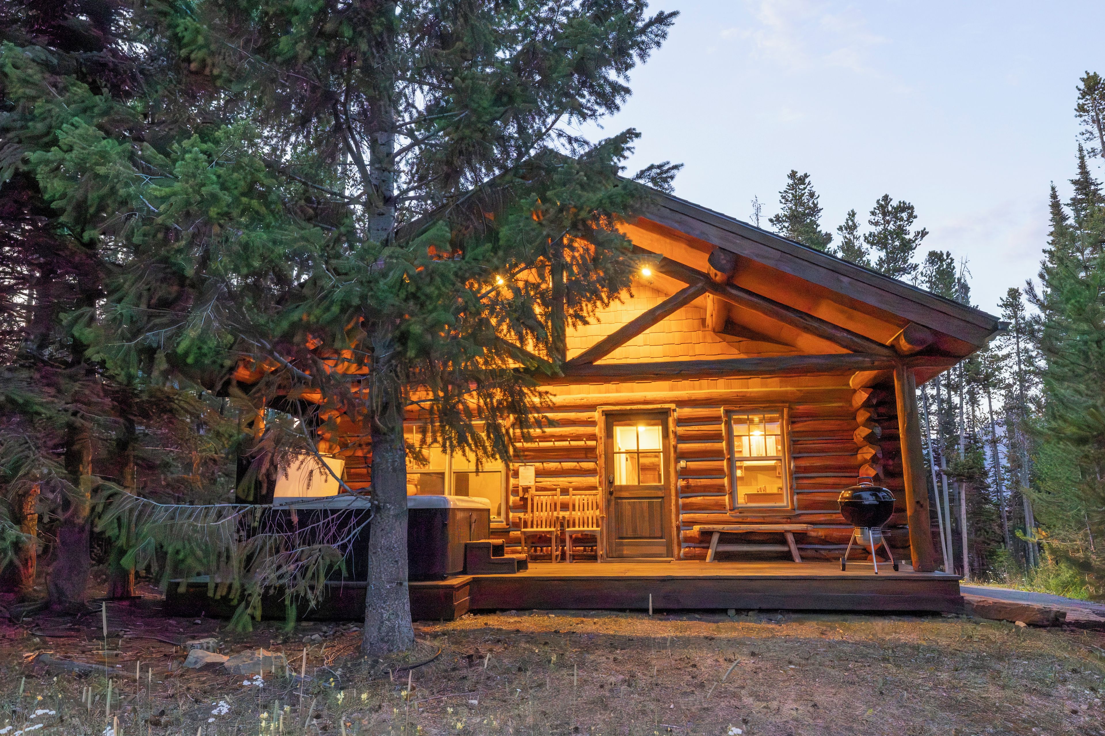 A log cabin with a porch, a bench, and a grill outside.