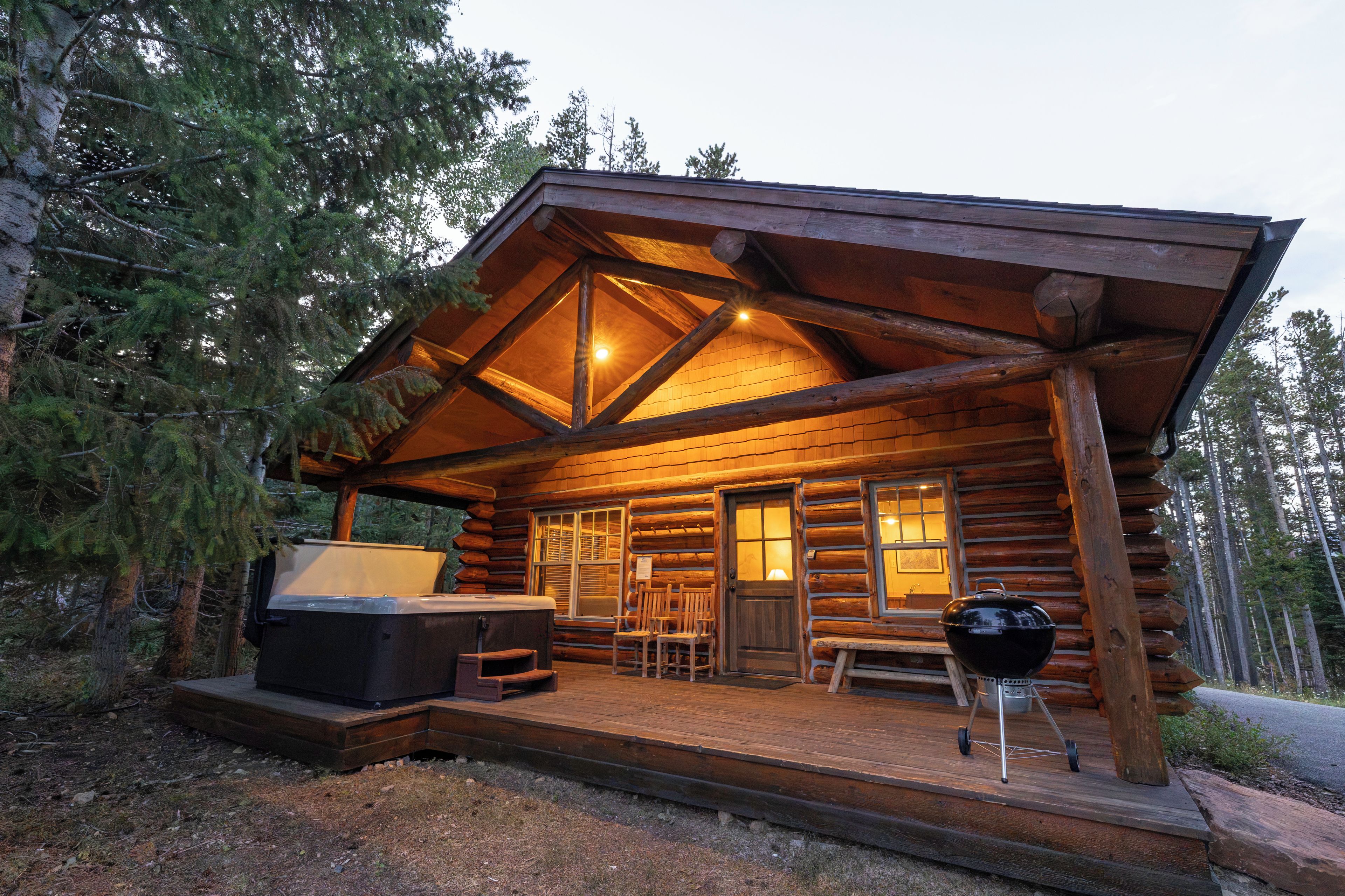 A log cabin with a porch, a hot tub, and a grill.