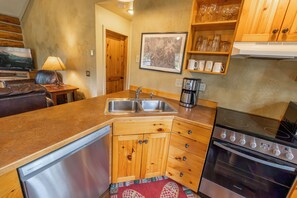 A compact kitchen with a dishwasher, double sink, coffee maker, and a stove. - NEW Stirrup Summit Cabin | Ski-In/Out 2BR Hot Tub (Big Sky)