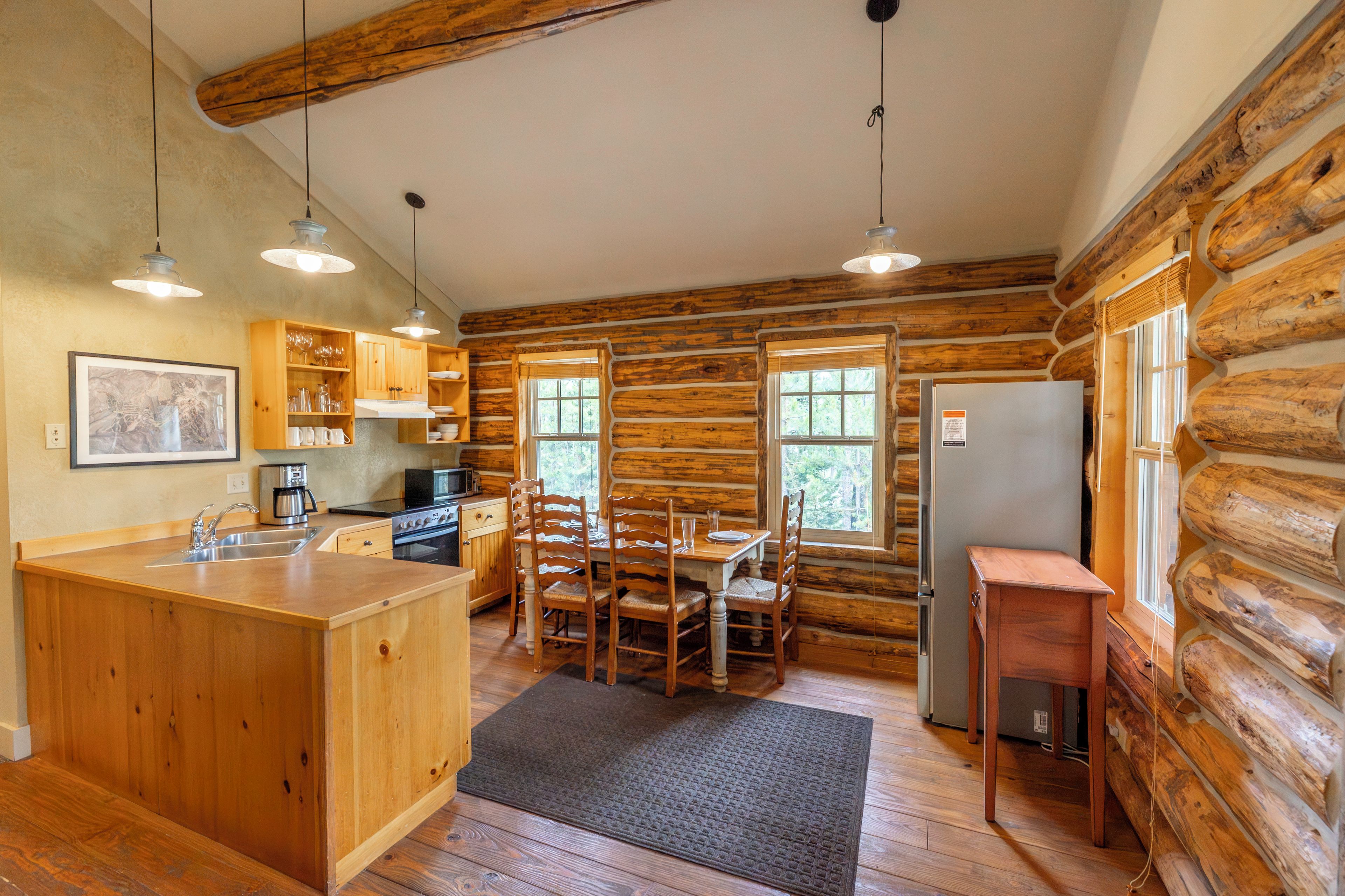 A log cabin interior with a kitchen, dining area, and a refrigerator.