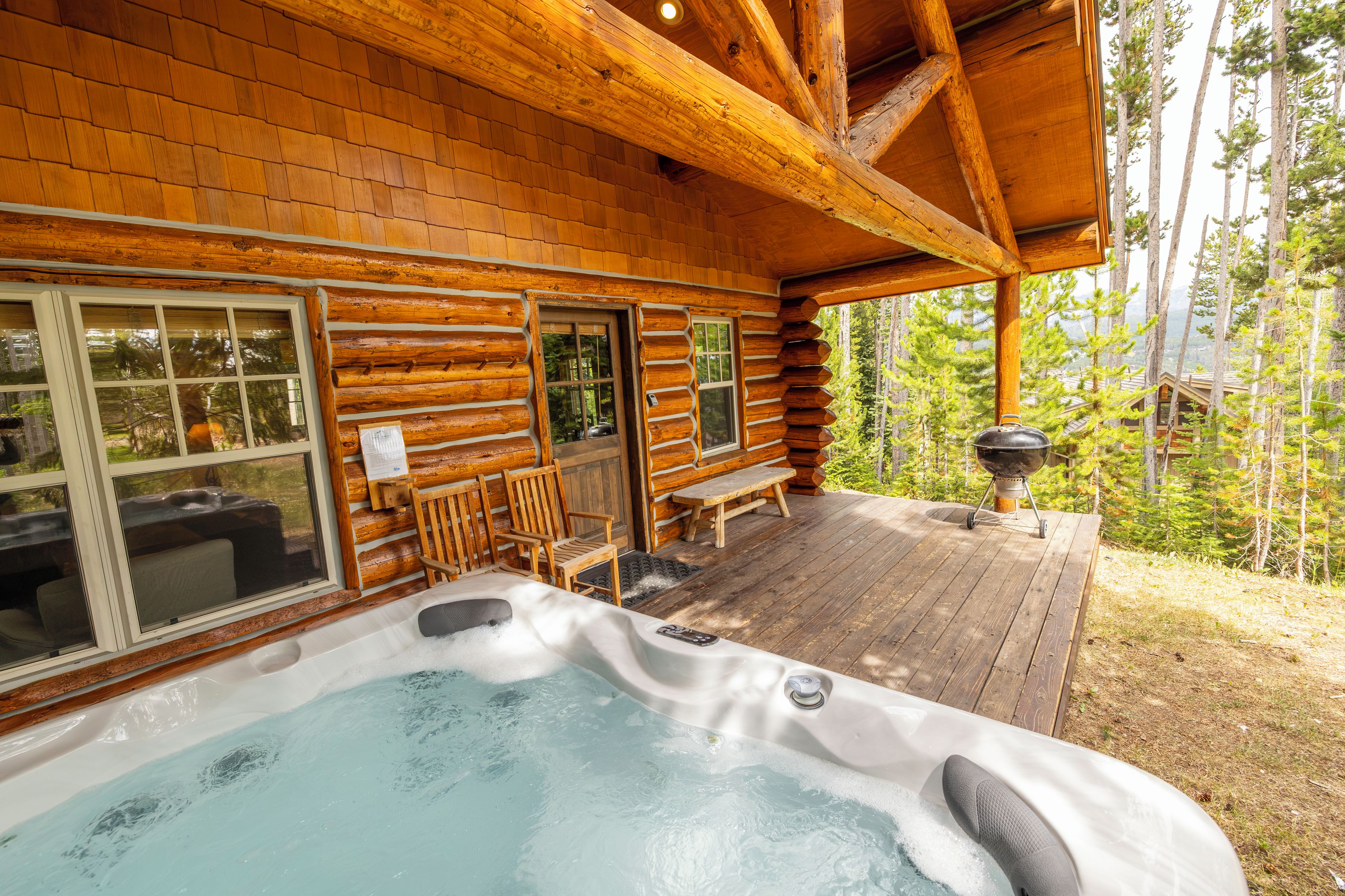 A log cabin with a hot tub, wooden deck, and a view of the forest.