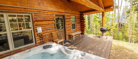 Uma cabana de tronco com hidromassagem, deck de madeira e vista para a floresta.