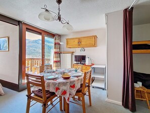 A dining area with a table set for four, a wooden cabinet above, and a view of the outdoors through a sliding door. - 2-room apartment at the slopes with balcony (Les Menuires)