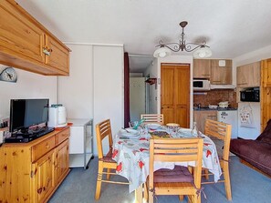 Cuina compacta amb armaris de fusta, taula de dinar amb cadires, televisió i microones.