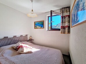 Un dormitori amb llit, finestra amb cortines, un quadre i una làmpada al sostre.