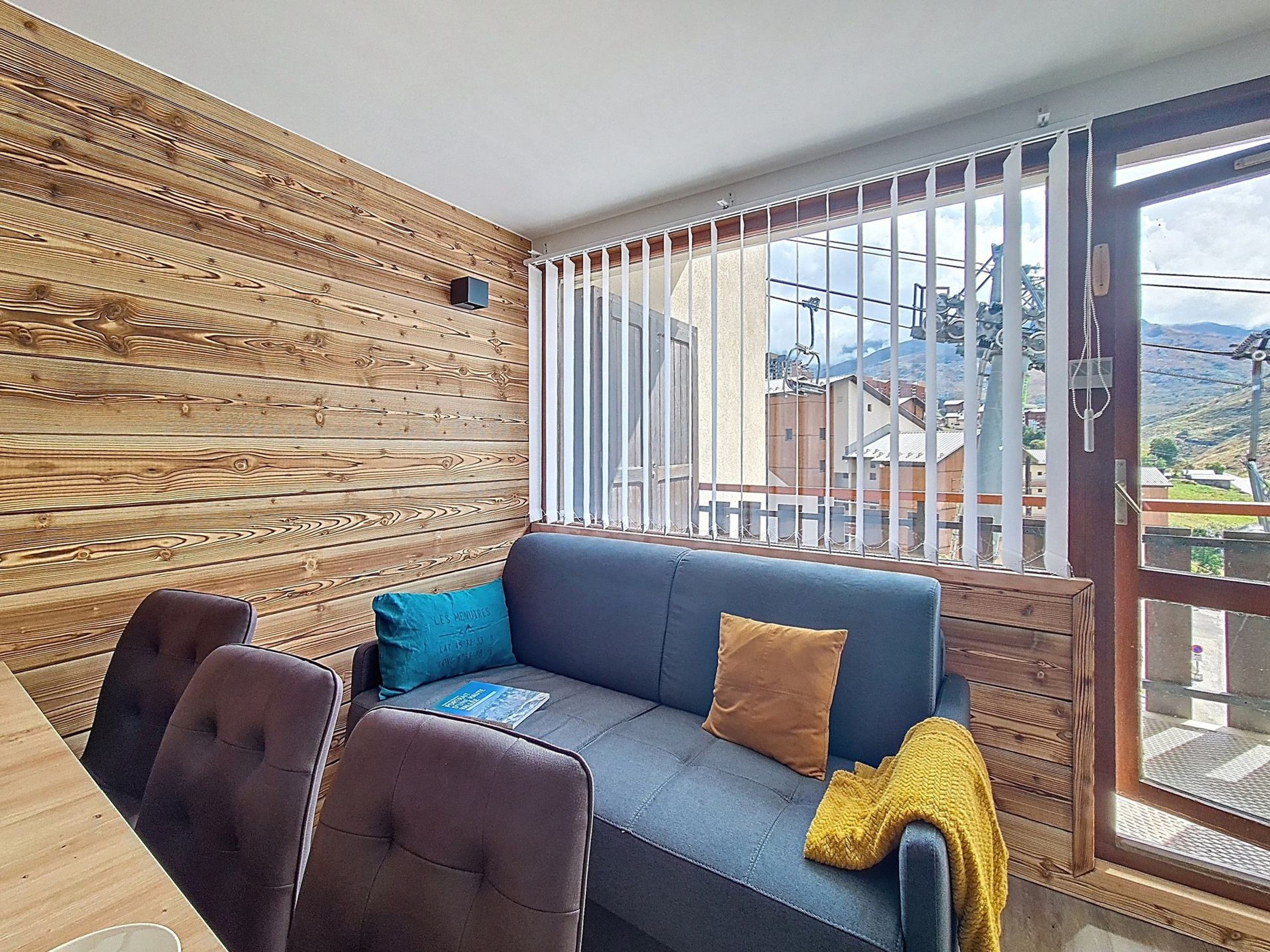 Une pièce avec un mur en bois, un canapé, deux fauteuils et une grande fenêtre donnant sur des immeubles et des montagnes.