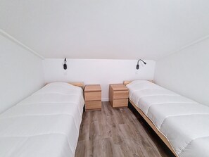 A twin room with two single beds, wooden nightstands, and wall-mounted reading lamps. - Renovated apartment, near slopes - 6 guests (Les Menuires)