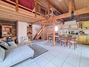 A spacious living area with a high ceiling, wooden beams, a sofa, a dining table with chairs, and a kitchen area. - Charming village house. Terrace. 5 min from St Martin de Belleville (Saint-Martin-de-Belleville)