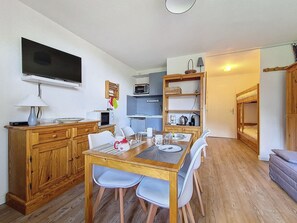 A compact living space with a dining area, kitchenette, and a television mounted on the wall. - Cozy studio with balcony, ski-in ski-out (Les Menuires)