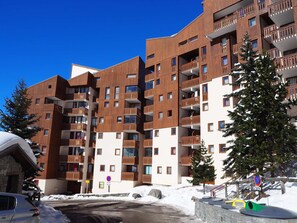 A multi-story building with balconies, a ski slope in the background, and snow on the ground. - Cozy studio with balcony, ski-in ski-out (Les Menuires)