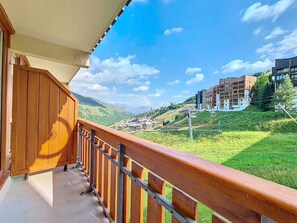 Een balkon met houten hekwerk met uitzicht op een bergachtig landschap met gebouwen.