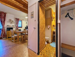 Ein Zimmer mit einem Holztisch, Stühlen, einem Fernseher und einer durch eine offene Tür einsehbarer Küchenbereich.