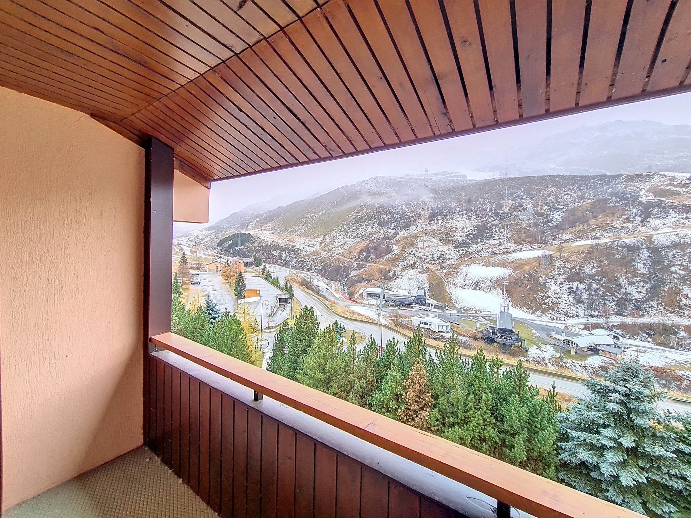 A balcony with a wooden railing overlooking a snowy landscape with buildings and trees.