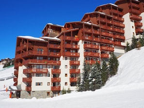 A multi-story hotel with wooden balconies and a snow-covered slope. - 3-room apartment, southwest balcony, at the foot of slopes (Les Menuires)