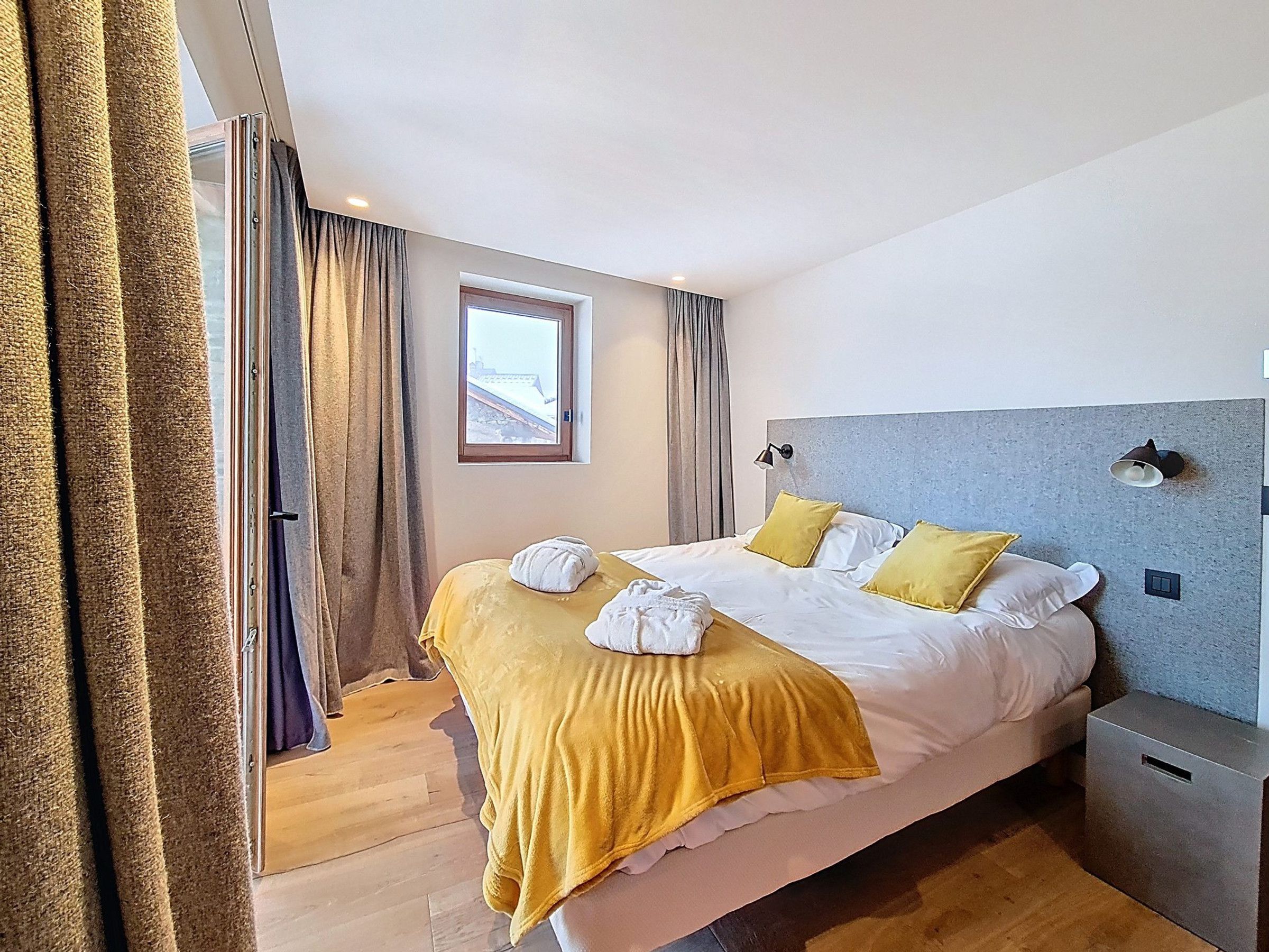 A hotel room with a bed, a window, curtains, and a nightstand.