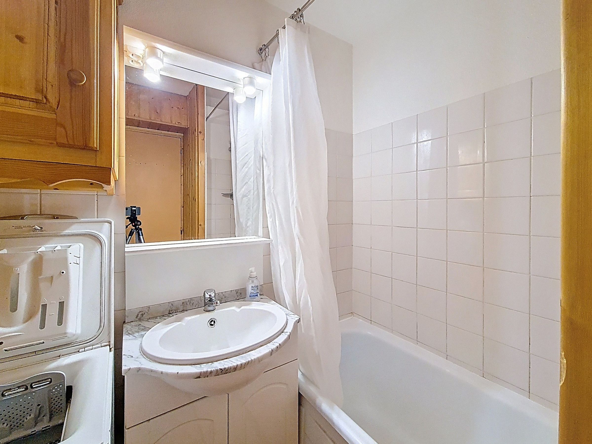 Un baño con un lavamanos blanco, un espejo, cortina de ducha y pared con azulejos.