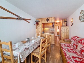 A dining area with a table set for four, wooden chairs, a red patterned sofa, and a kitchen in the background. - Spacious apartment - 6 guests at the foot of the slopes (Les Menuires)