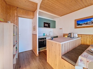 A compact kitchen with wooden cabinetry, a built-in oven, and a small island with seating. - Bright apartment for 5. Close to slopes. Balcony. (Les Menuires)