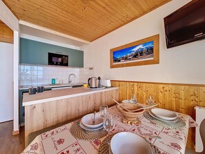 A kitchen with a wooden ceiling, a dining area with a table set for two, and a mounted television. - Bright apartment for 5. Close to slopes. Balcony. (Les Menuires)