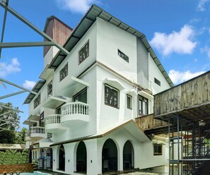 Una casa de varios pisos con un balcón, arcos y una piscina.