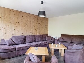 Un salon moderne avec un mur lambrissé en bois, un canapé d’angle, une table basse et un luminaire suspendu.