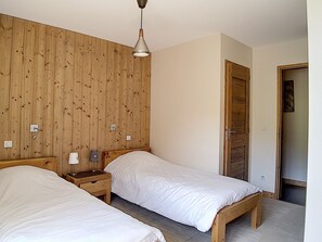 A bedroom with two beds, wooden walls, a nightstand with a lamp, and a door. - Spacious 7-room apartment near slopes with sauna, hammam, and wifi (Les Menuires)