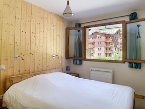 Une chambre à coucher avec un lit, des murs recouverts de panneaux de bois, une fenêtre avec des rideaux et une vue sur un bâtiment à l’extérieur.