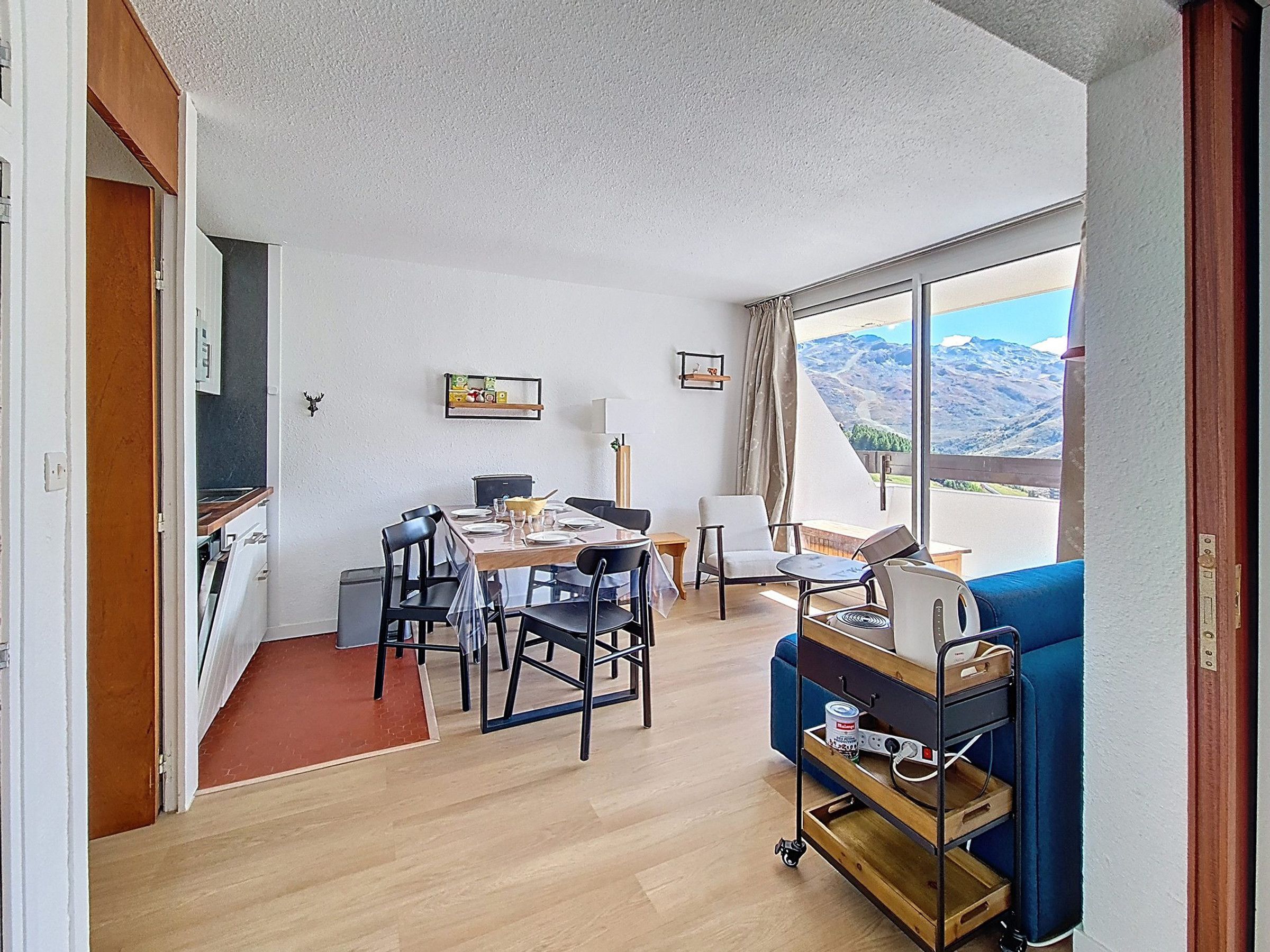 Una stanza con un tavolo da pranzo, sedie, un divano, un carrello con oggetti vari e un'ampia finestra vista montagna.