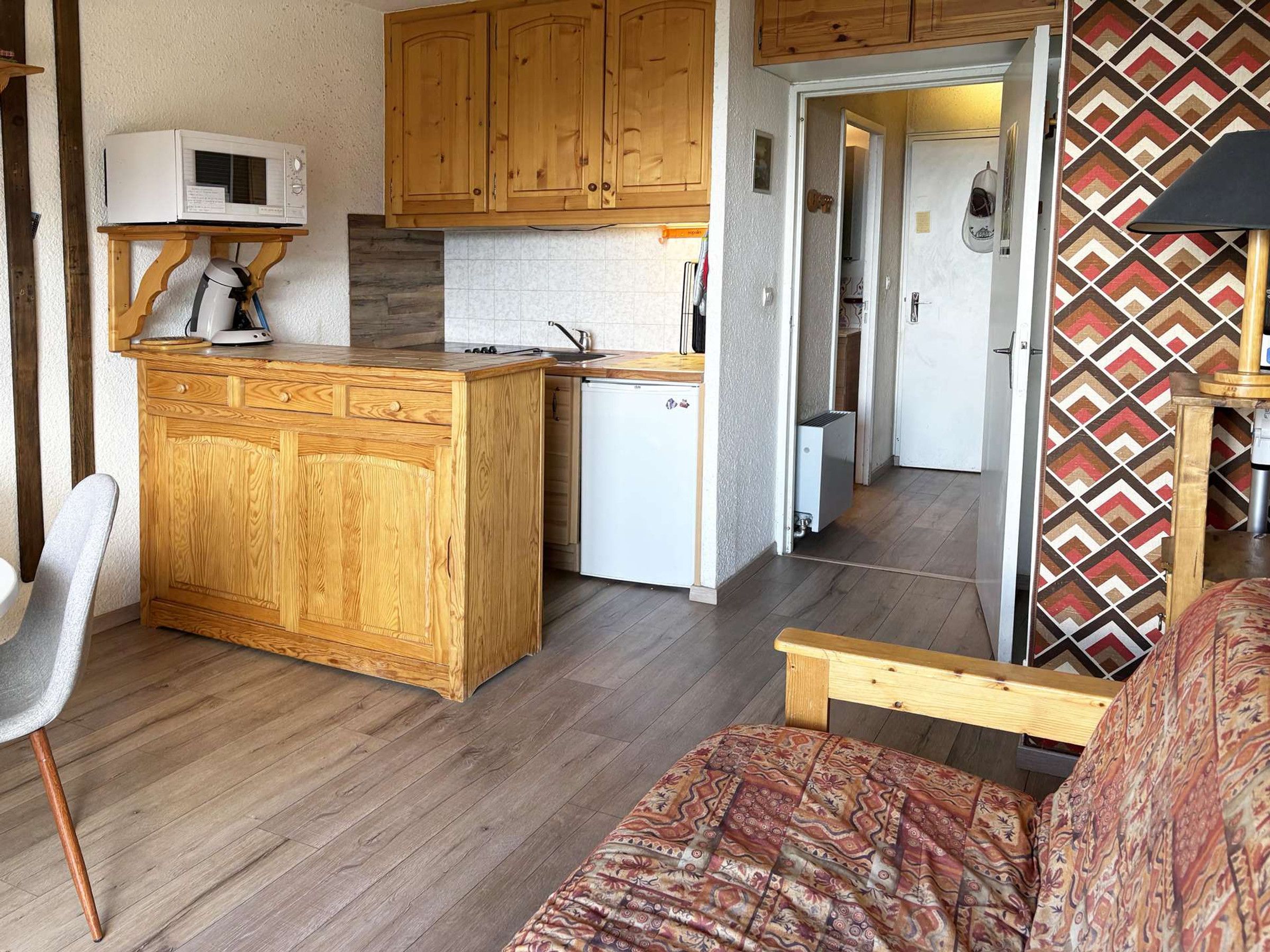 Een compacte keuken met houten kastjes, een magnetron, een kleine koelkast en een koffiezetapparaat op een houten tafel.