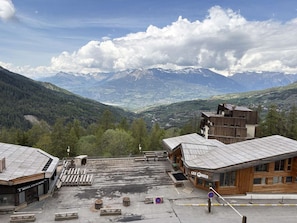 A hotel with a wooden facade, a parking area, and a view of mountains. - Cozy studio in the heart of the resort - 4 guests (Les Orres)