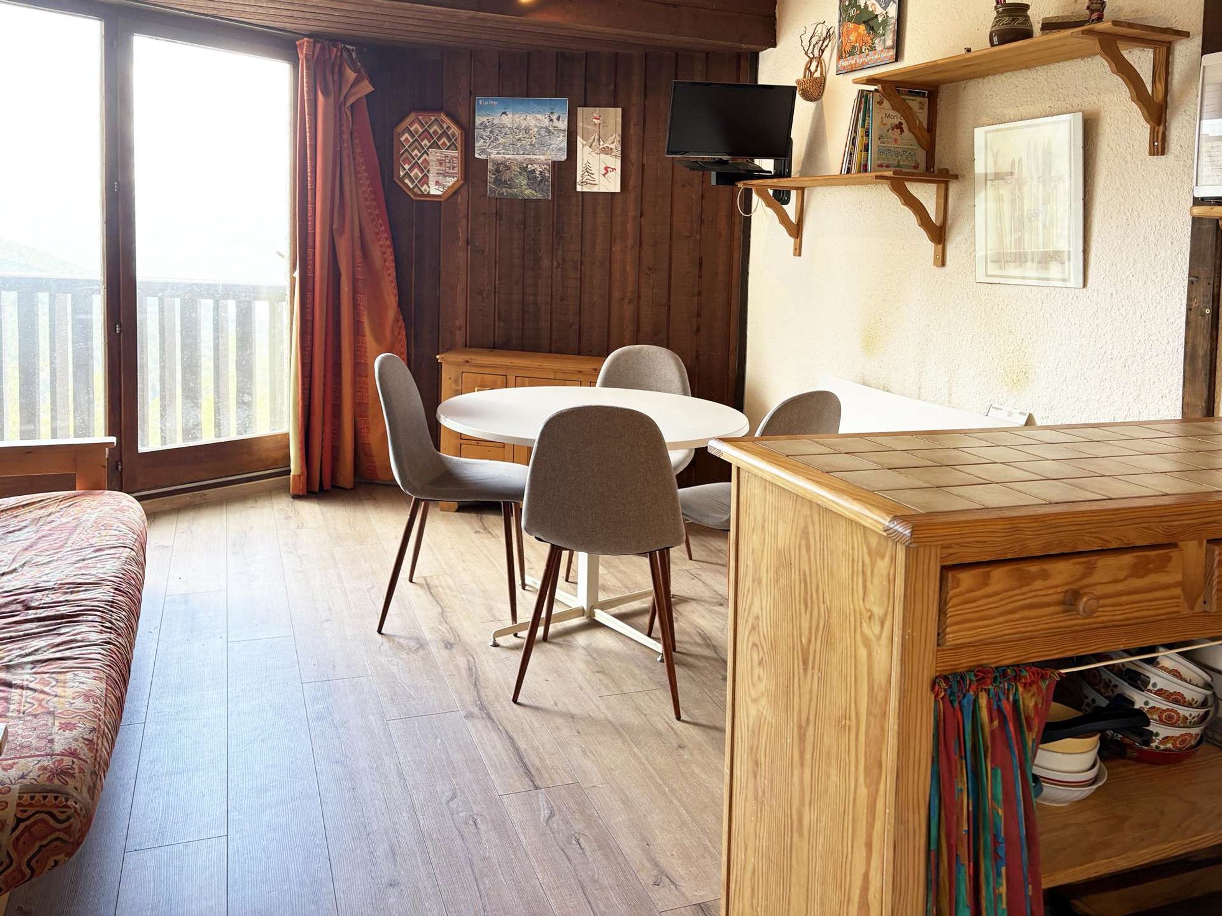 Ein gemütliches Zimmer mit einem Holzesstisch, Stühlen, einem Fernseher und einem Fenster mit Vorhängen.
