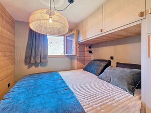 A bedroom with a bed, a window, a hanging light fixture, and wooden walls. - Renovated apartment with balcony, ski-in/ski-out, 4 people (Les Menuires)
