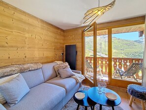 A wooden cabin interior with a sofa, a table with glasses, and a balcony with chairs. - Renovated apartment with balcony, ski-in/ski-out, 4 people (Les Menuires)