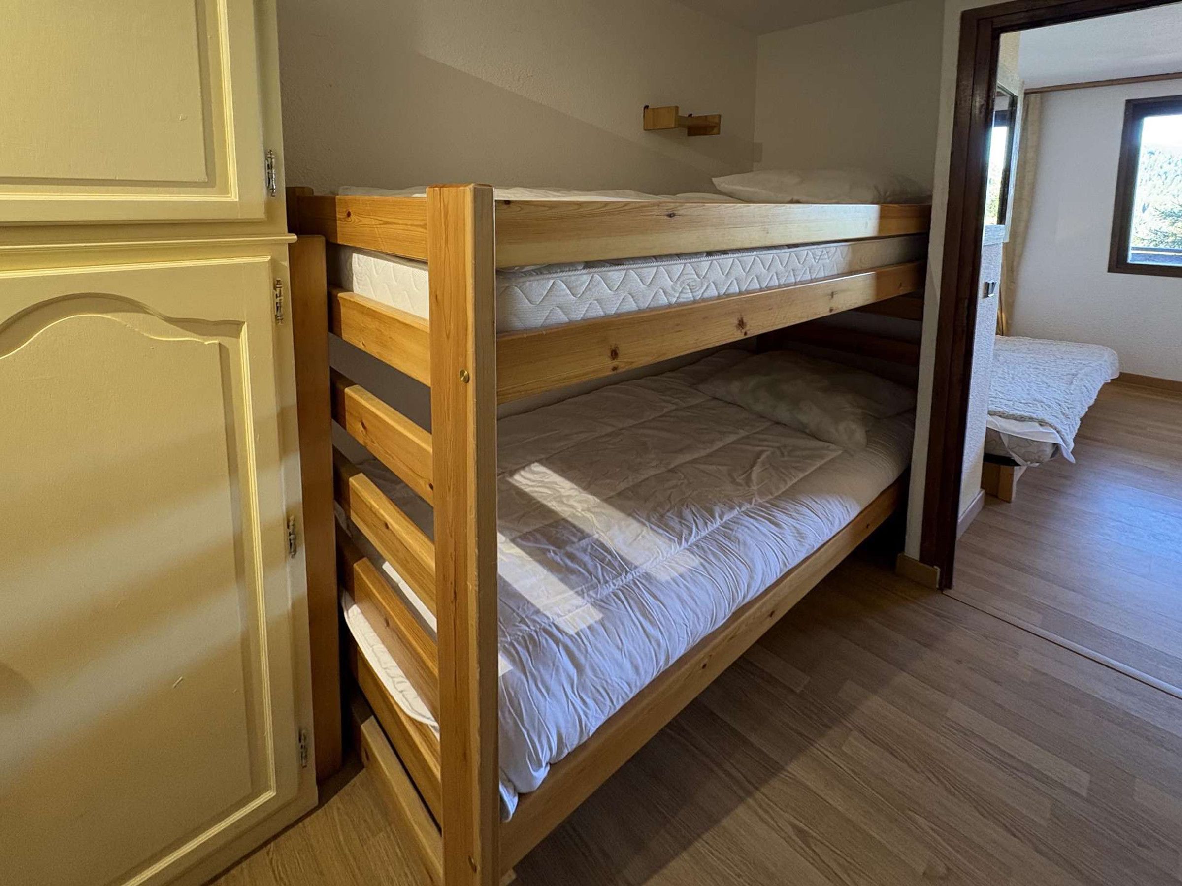 A bunk bed with a wooden frame, a white mattress, and a wooden door with a decorative panel.