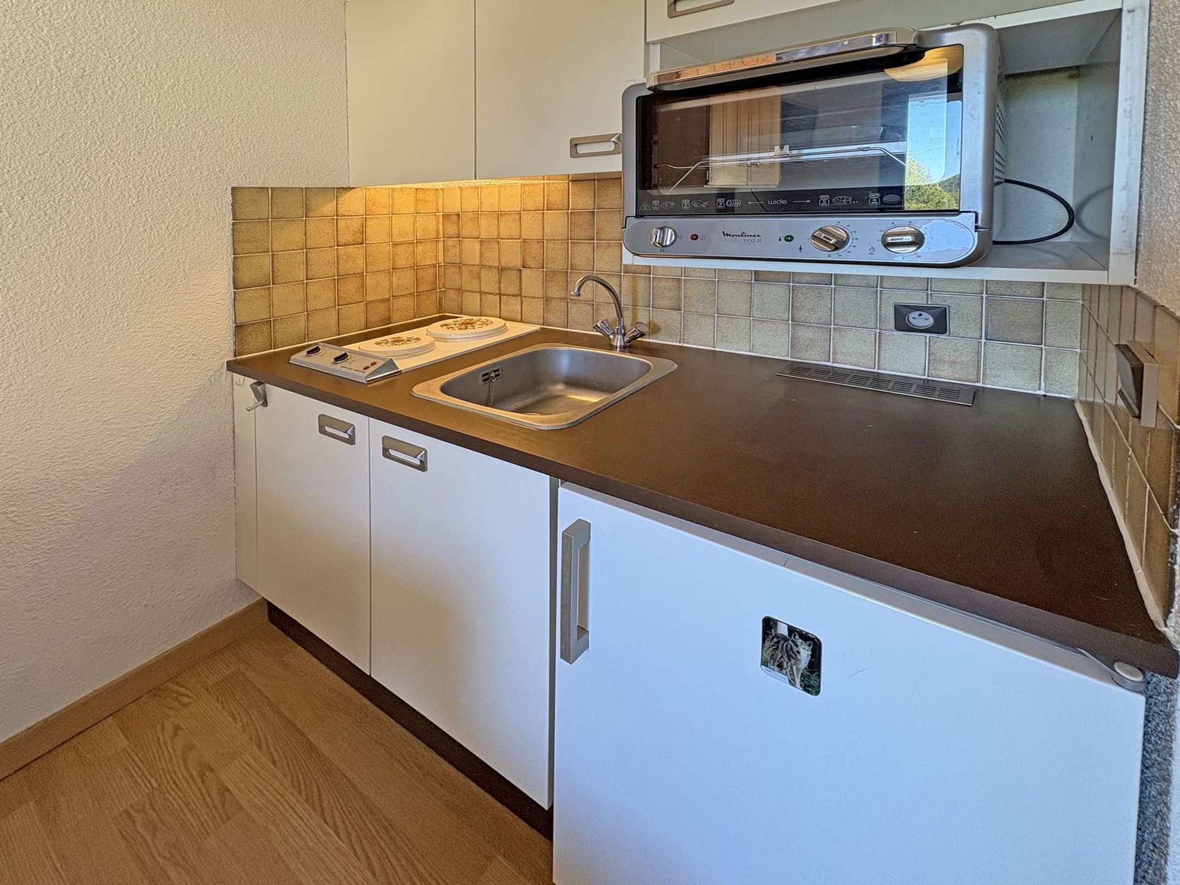 Eine kleine Küchenzeile mit einem eingebauten Toaster, einer Spüle und weißen Schränken.