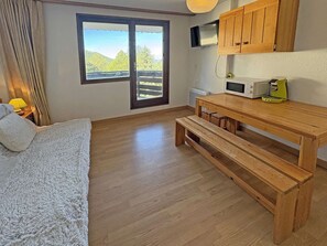 Een kamer met een bed, een houten bankje, een tafel, een televisie en uitzicht door een raam.
