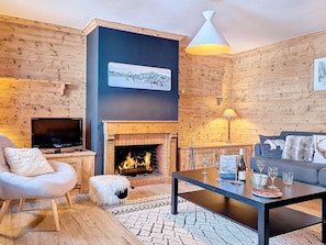 Ein gemütliches Wohnzimmer mit Kamin, einer Couch, einem Couchtisch und einem Fernseher.