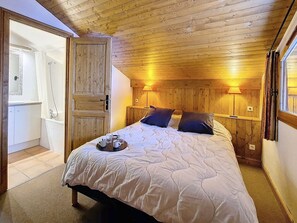 Ein Schlafzimmer mit Holzboden, einem Bett mit weißer Bettwäsche, zwei Nachttischlampen und einer Tür zu einem Badezimmer.