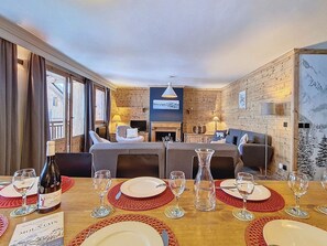 Ein Essbereich mit einem Holztisch, gedeckt für eine Mahlzeit, einem Kamin und einem Wohnbereich mit Sofas und einem Fernseher.