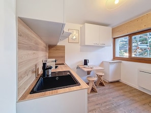 A compact kitchen with a black sink, wooden countertop, and a small table with stools. - Renovated studio at the slopes with WIFI (Les Menuires)