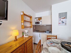 Una kitchenette compacta con microondas, cafetera y un estante de madera sobre la encimera.