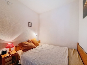 Un dormitorio con una cama, una mesita de noche, una lámpara roja y un aplique de pared.