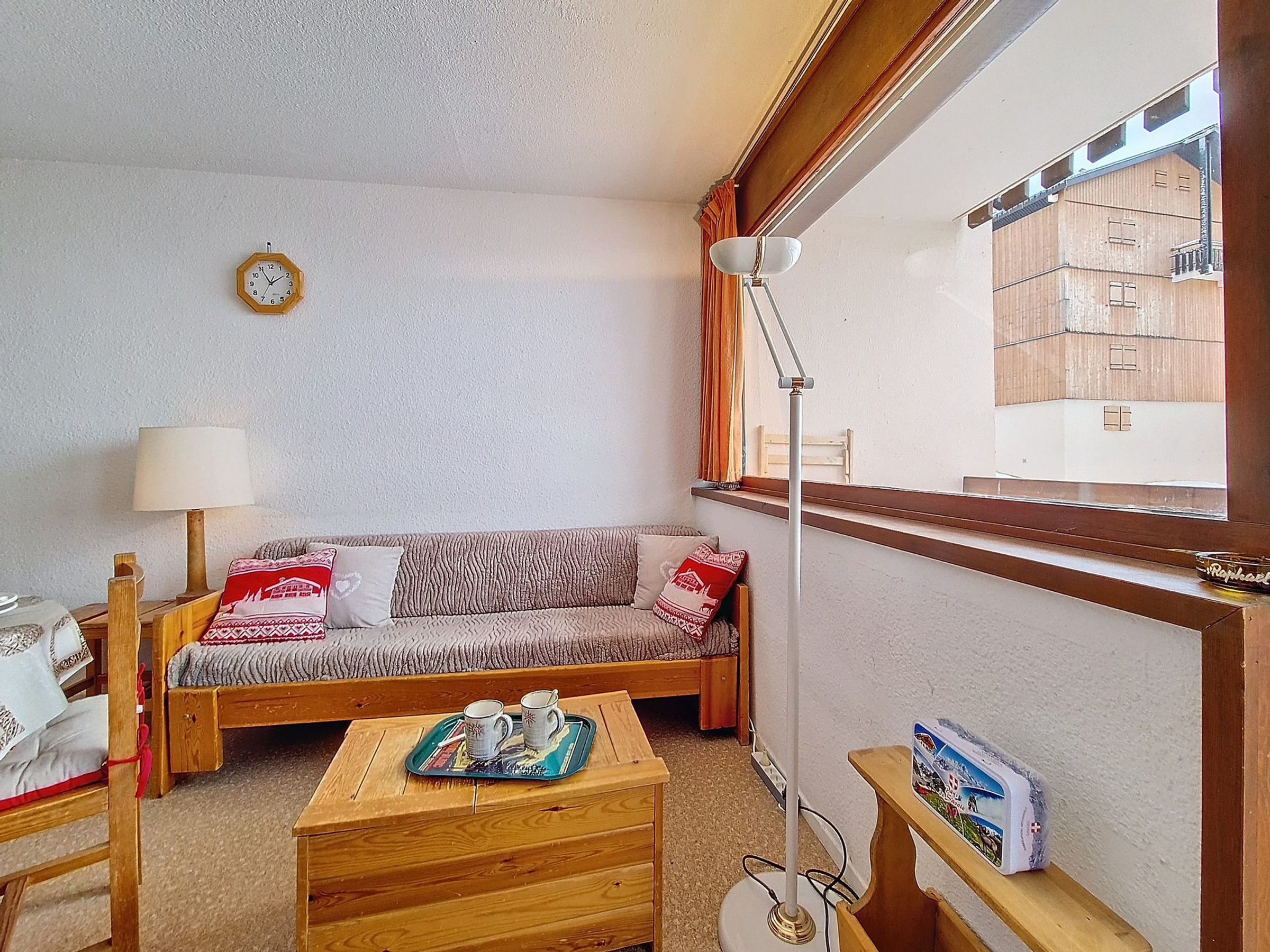 A cozy room with a sofa, a small wooden table with a tray, a lamp, and a window with a view of buildings.
